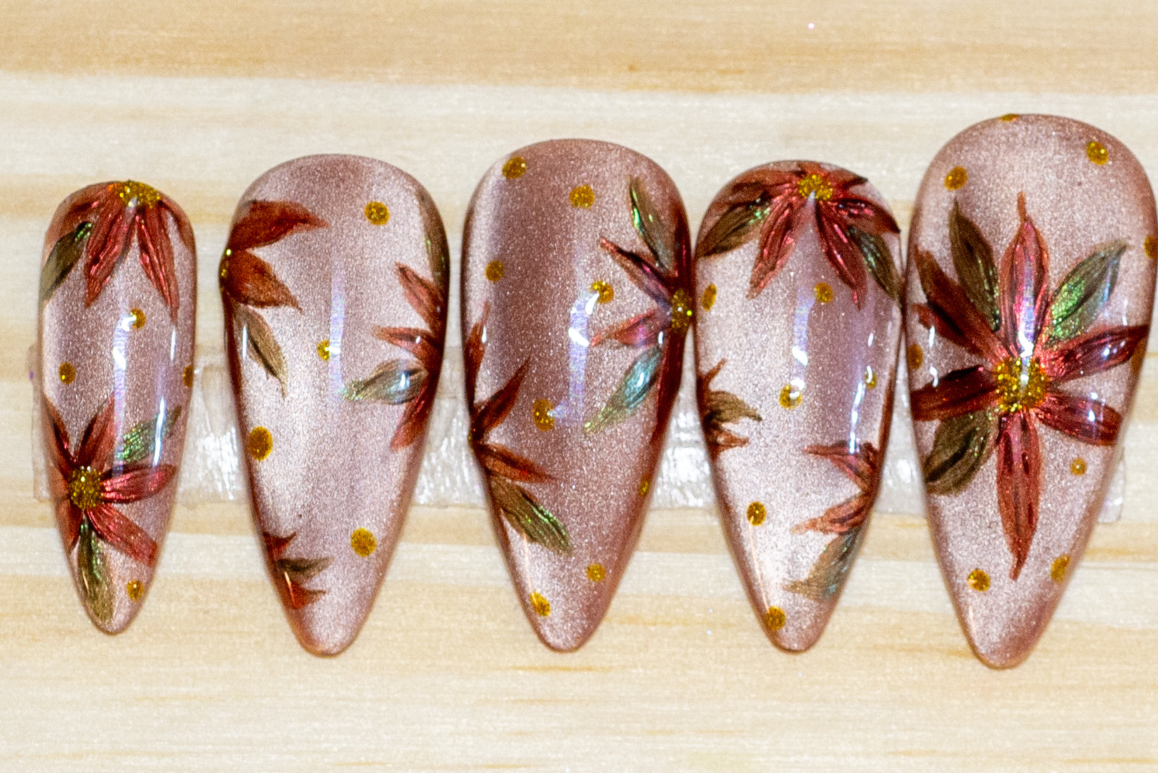 Hand-painted press on nails with chromed poinsettias on a neutral cateye base, featured on a wooden background