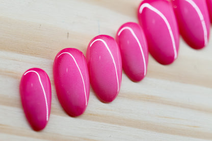 Deep pink press on nails with lighter pink aura design featured on a wooden background