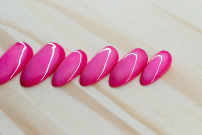 Deep pink press on nails with lighter pink aura design featured on a wooden background