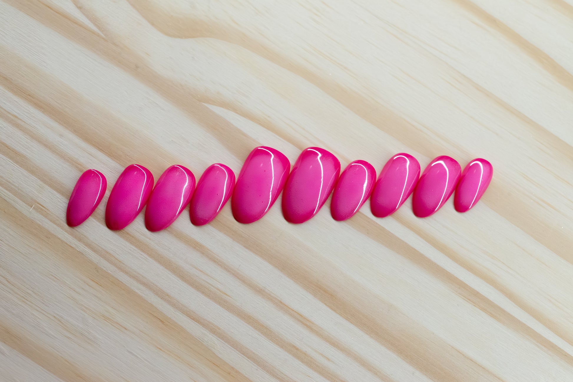Deep pink press on nails with lighter pink aura design featured on a wooden background