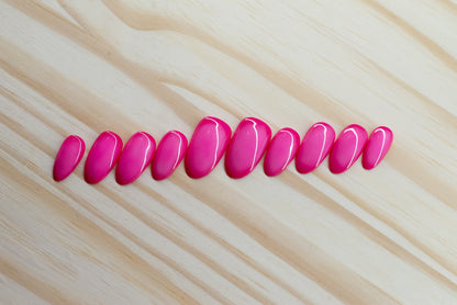 Deep pink press on nails with lighter pink aura design featured on a wooden background