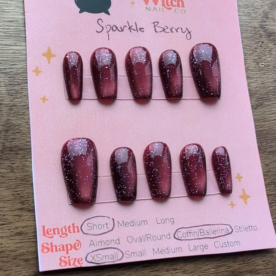 Video showing the deep berry pink cat eye effect press on nails with holographic glitter on a pink card