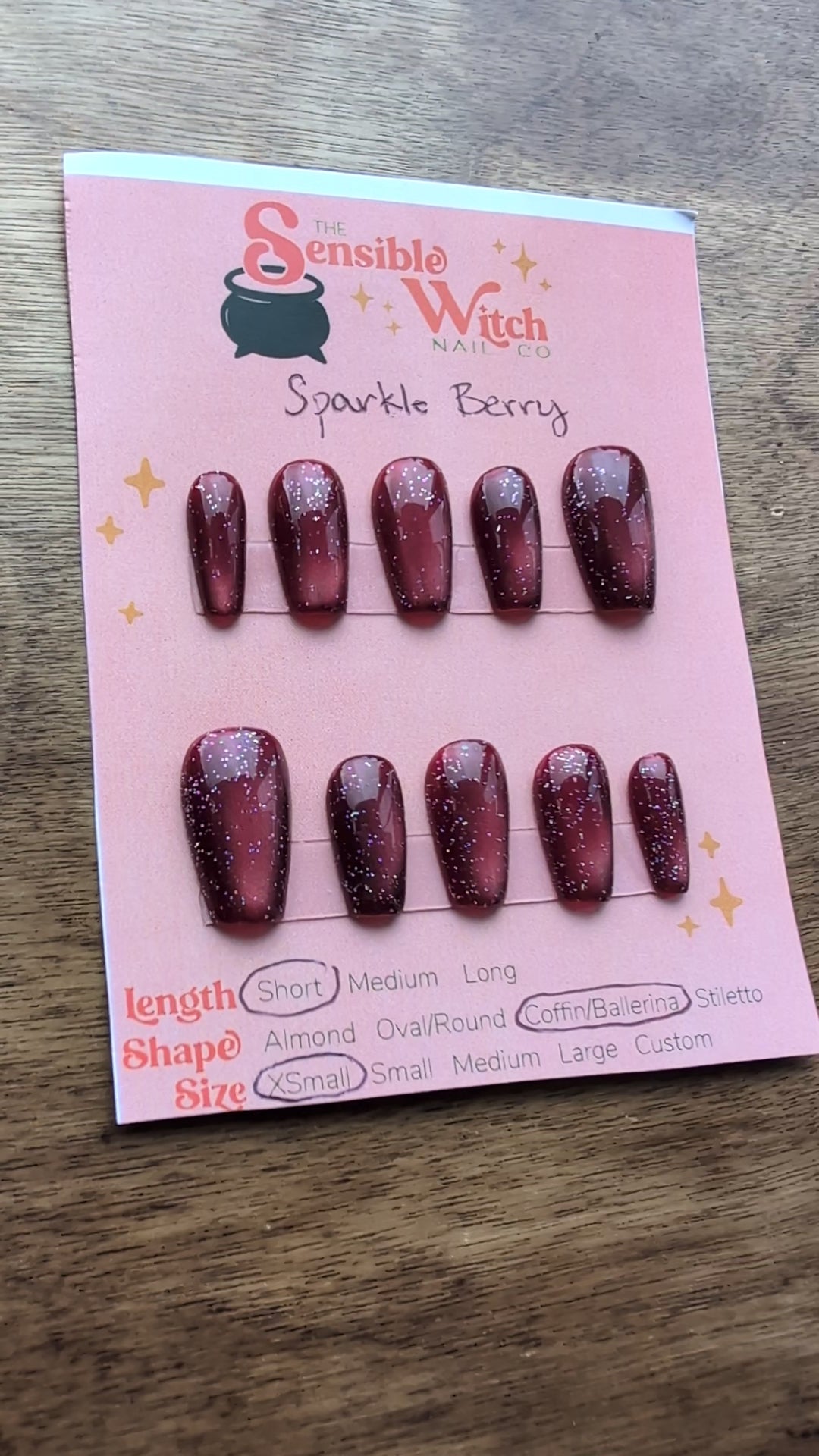 Video showing the deep berry pink cat eye effect press on nails with holographic glitter on a pink card