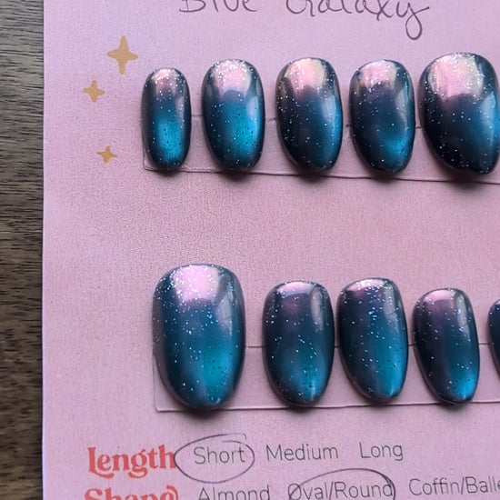 Video of set of blue galaxy cateye press on nails on a card with pink background