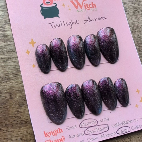 Video featuring cat eye press on nails in purple/fuchsia with teal green french tip flash on a pink card