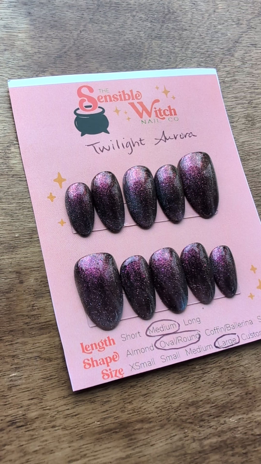Video featuring cat eye press on nails in purple/fuchsia with teal green french tip flash on a pink card