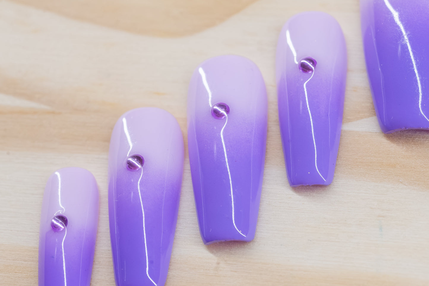 royal purple to lavender ombre press on nails with single rhinestone each featured on a wooden background