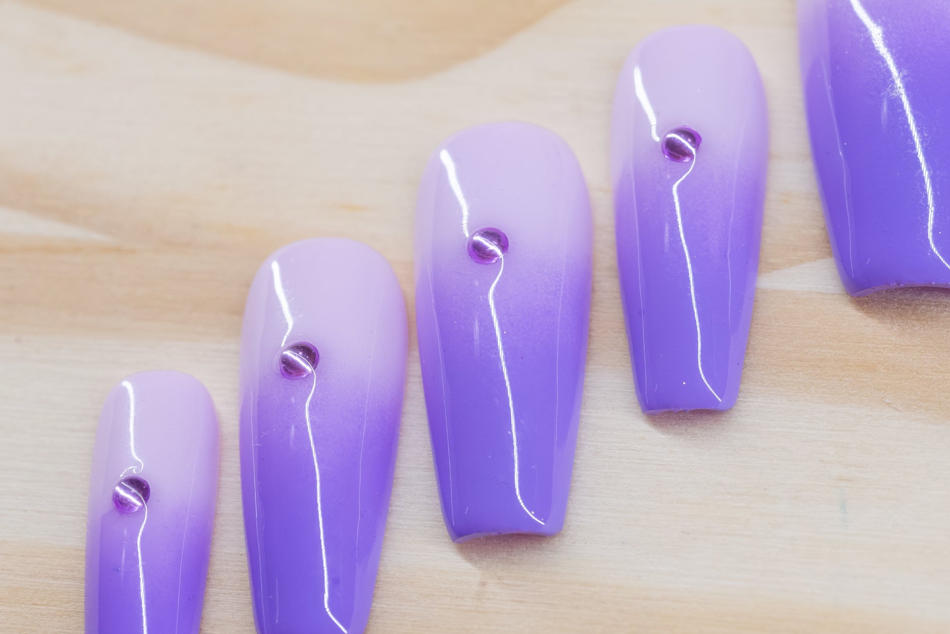 royal purple to lavender ombre press on nails with single rhinestone each featured on a wooden background
