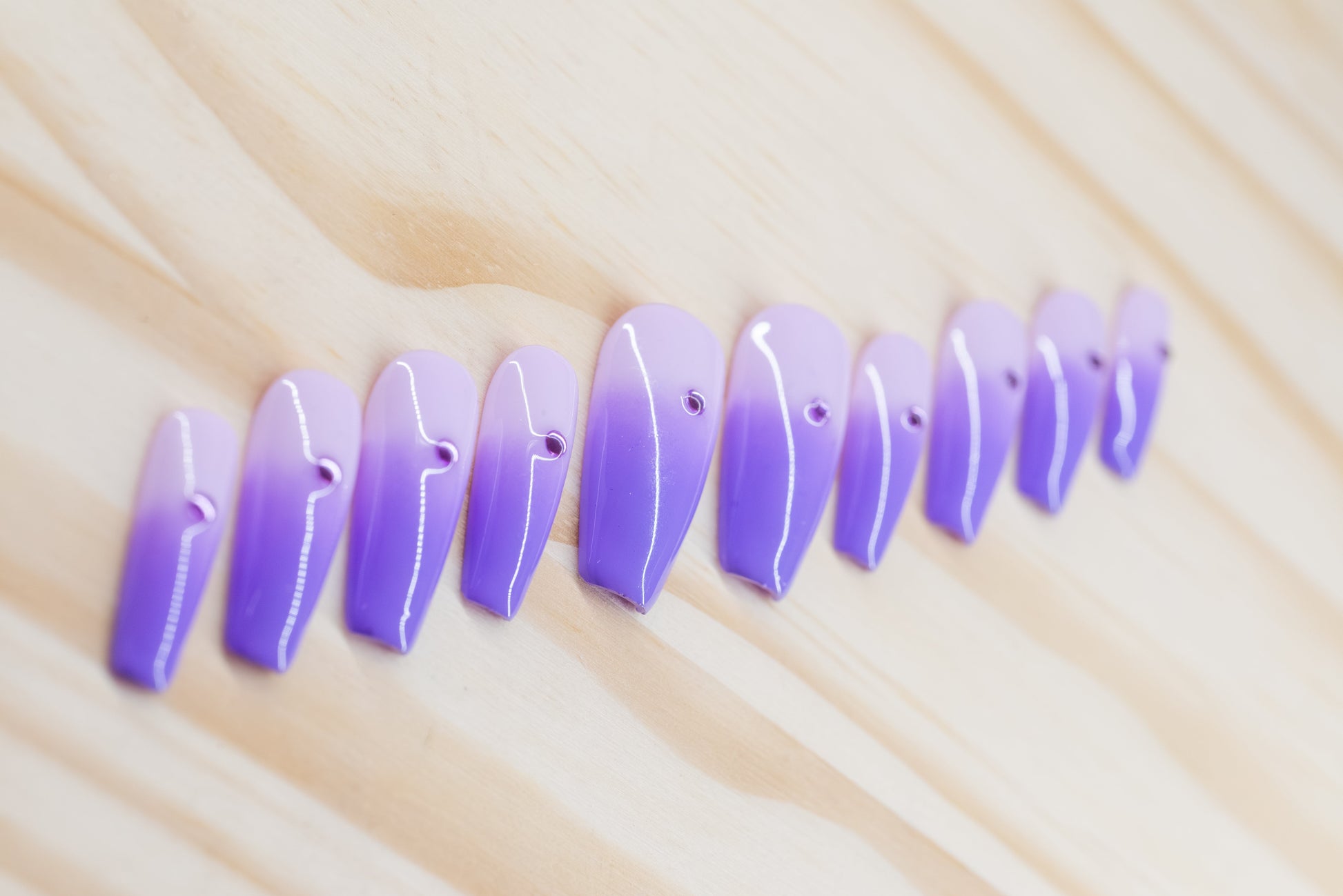 royal purple to lavender ombre press on nails with single rhinestone each featured on a wooden background