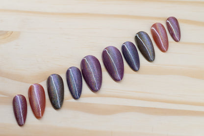 press on nails in jewel toned purple, blue, green, yellow, and red with holographic cat eye overlay featured on a wooden background