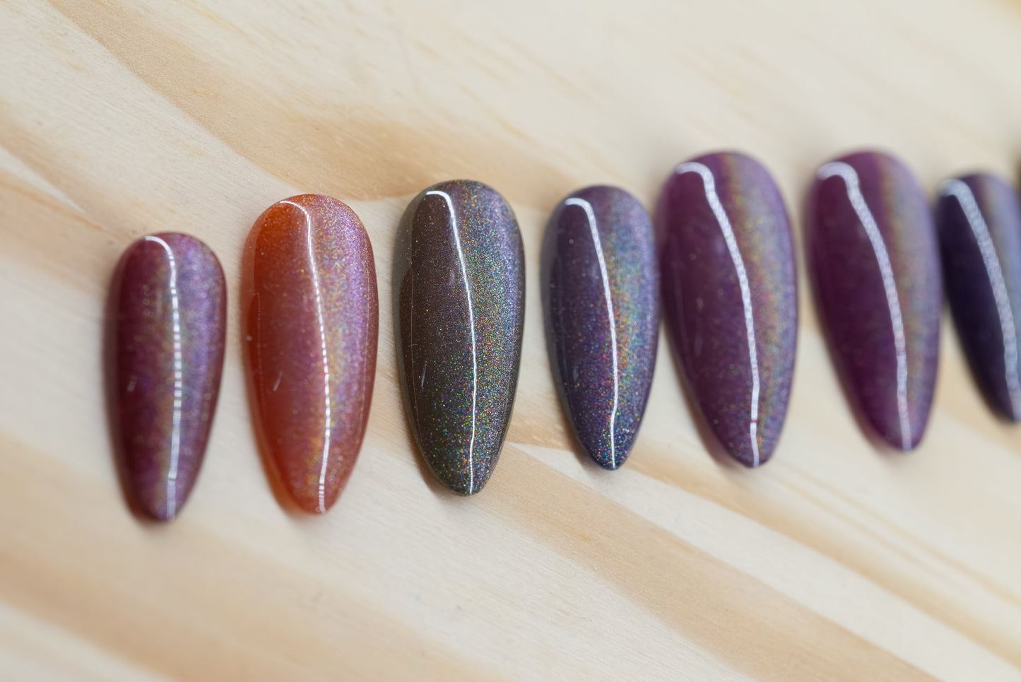 press on nails in jewel toned purple, blue, green, yellow, and red with holographic cat eye overlay featured on a wooden background