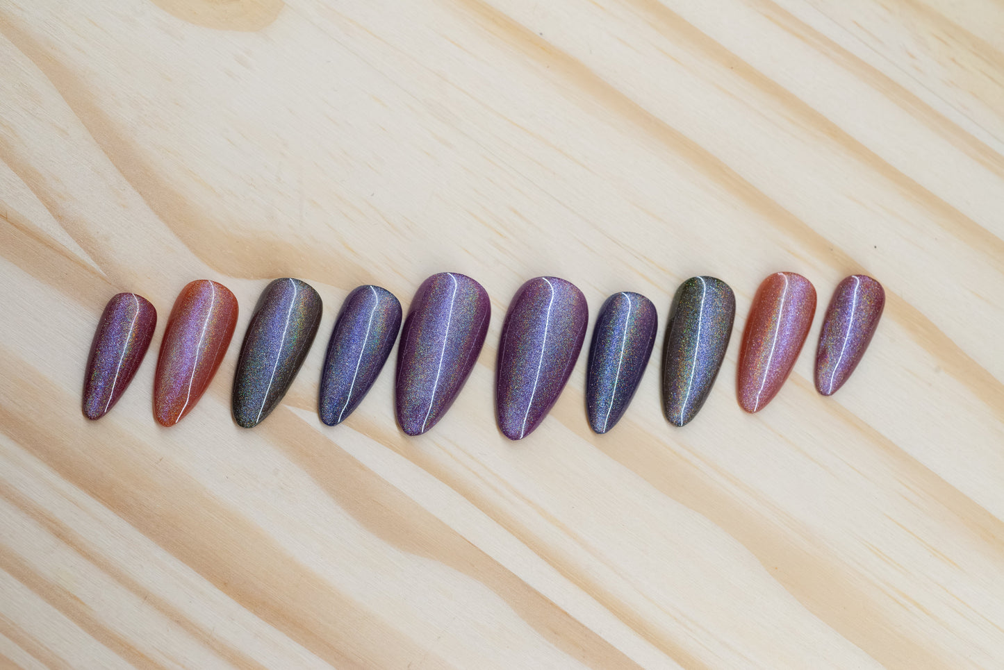 press on nails in jewel toned purple, blue, green, yellow, and red with holographic cat eye overlay featured on a wooden background