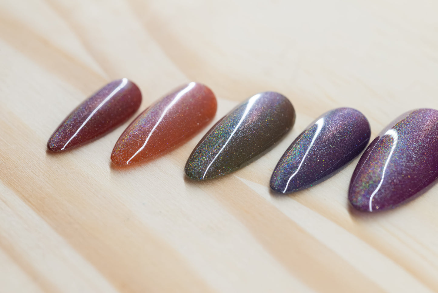 press on nails in jewel toned purple, blue, green, yellow, and red with holographic cat eye overlay featured on a wooden background