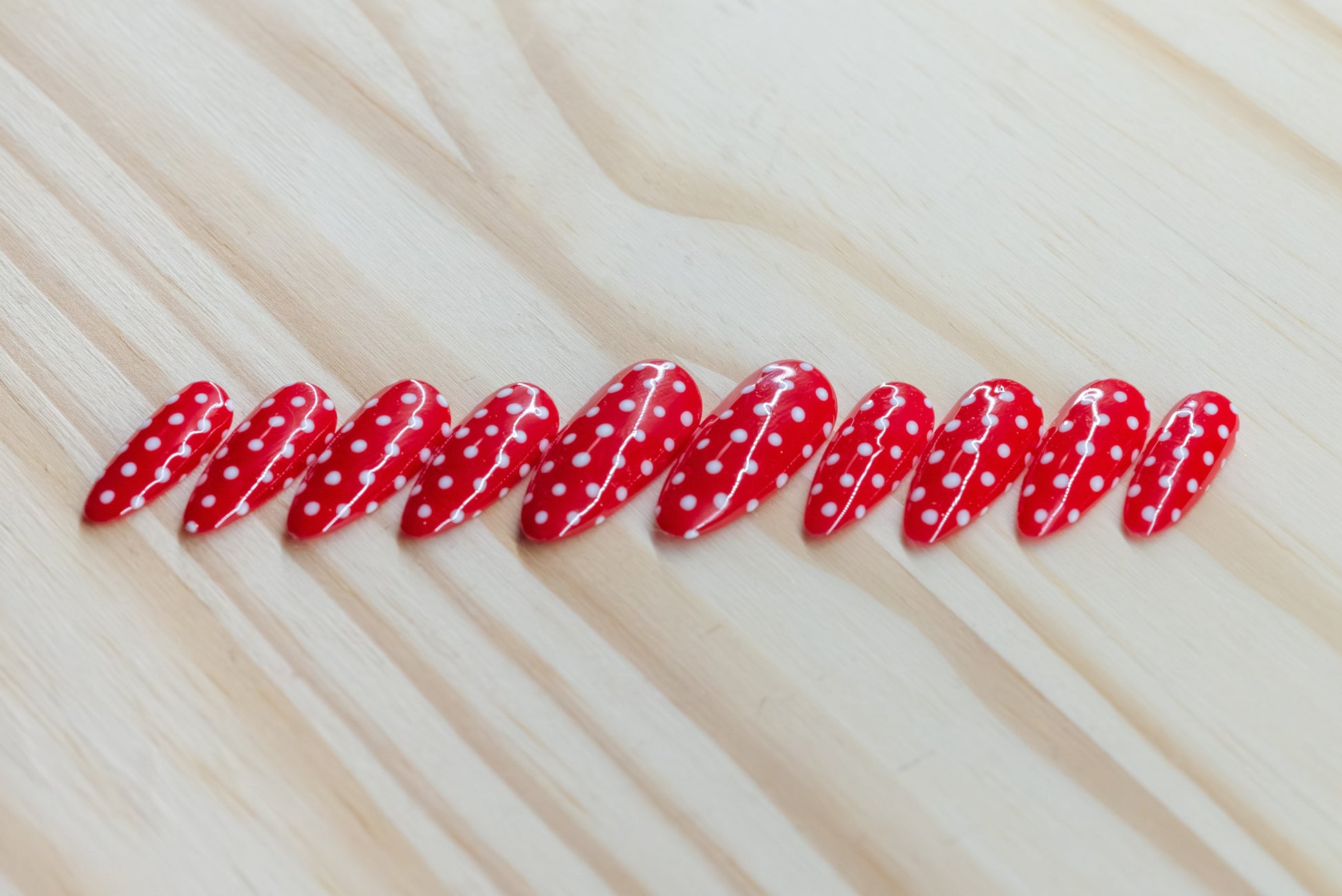 red press on nails with white polka dots on a wooden background