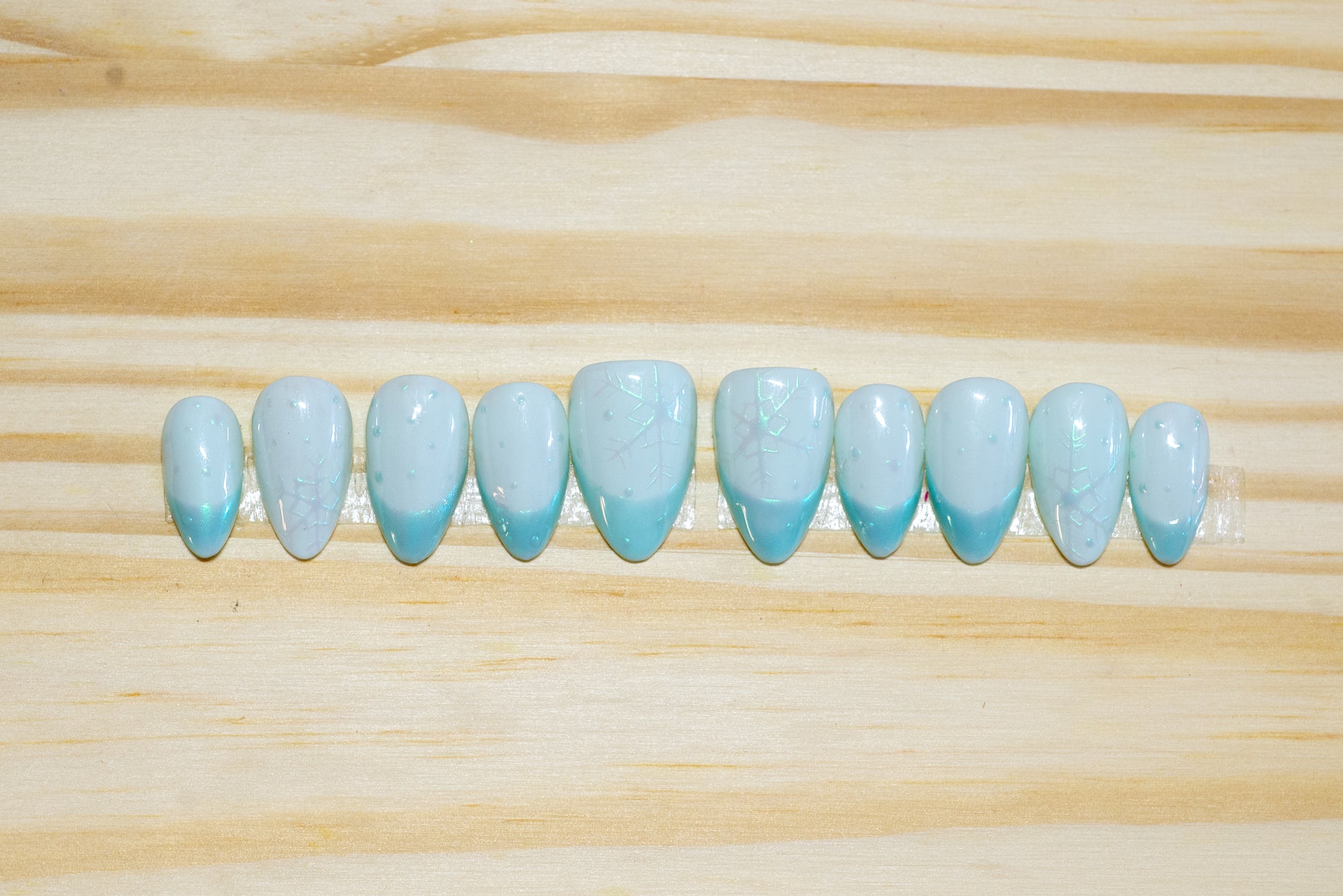 pale blue press on nails with irridescent snowflakes and darker blue irridescent french tips on a wooden background