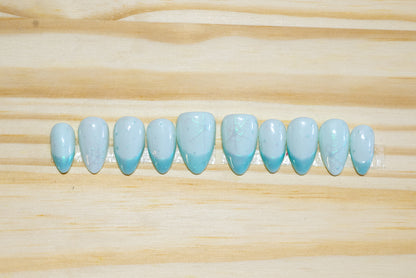 pale blue press on nails with irridescent snowflakes and darker blue irridescent french tips on a wooden background