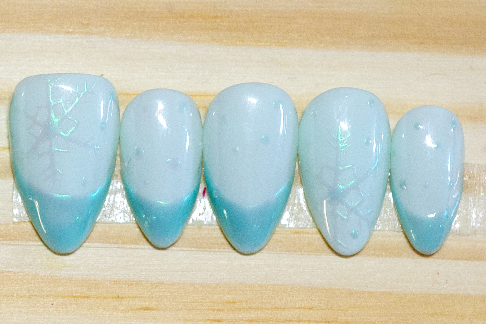 pale blue press on nails with irridescent snowflakes and darker blue irridescent french tips on a wooden background