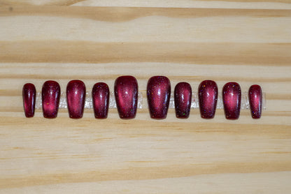 Sparkly berry-red cat eye press-on nails on a wooden background