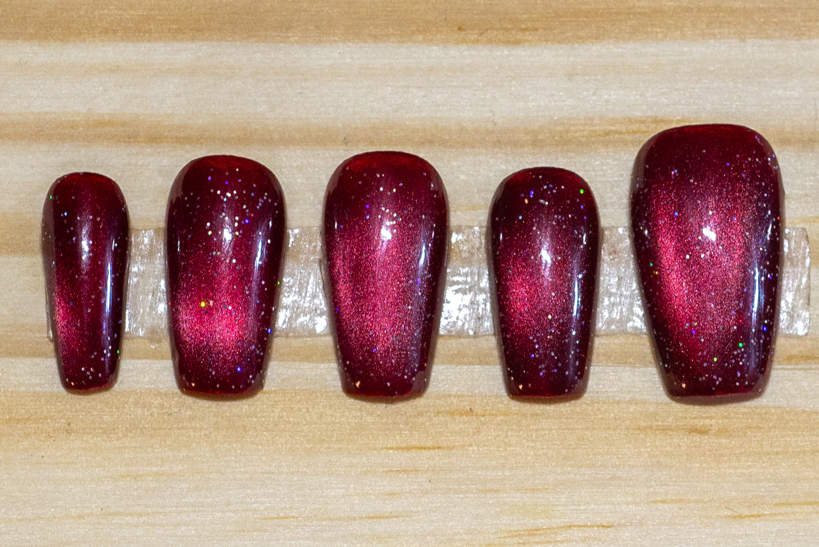 Sparkly berry-red cat eye press-on nails on a wooden background