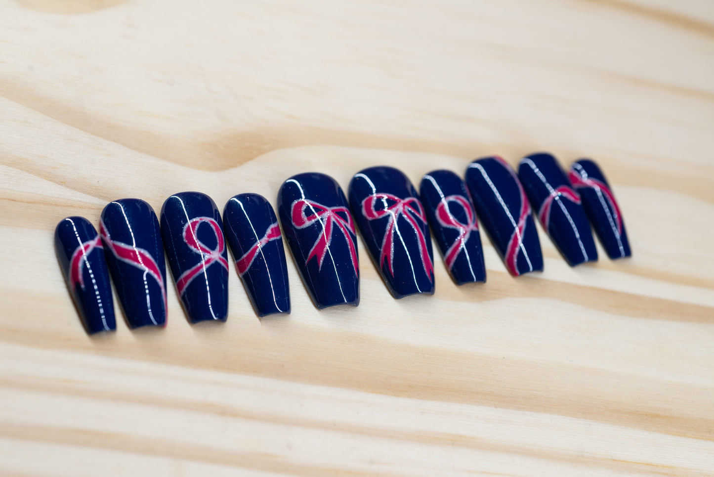 navy blue press on nails with pink bow motif featured on a wooden background