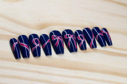 navy blue press on nails with pink bow motif featured on a wooden background
