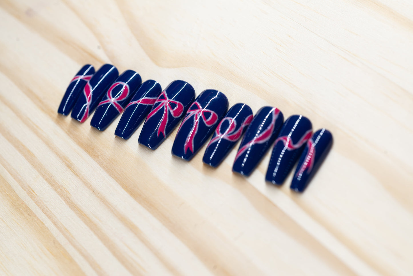 navy blue press on nails with pink bow motif featured on a wooden background