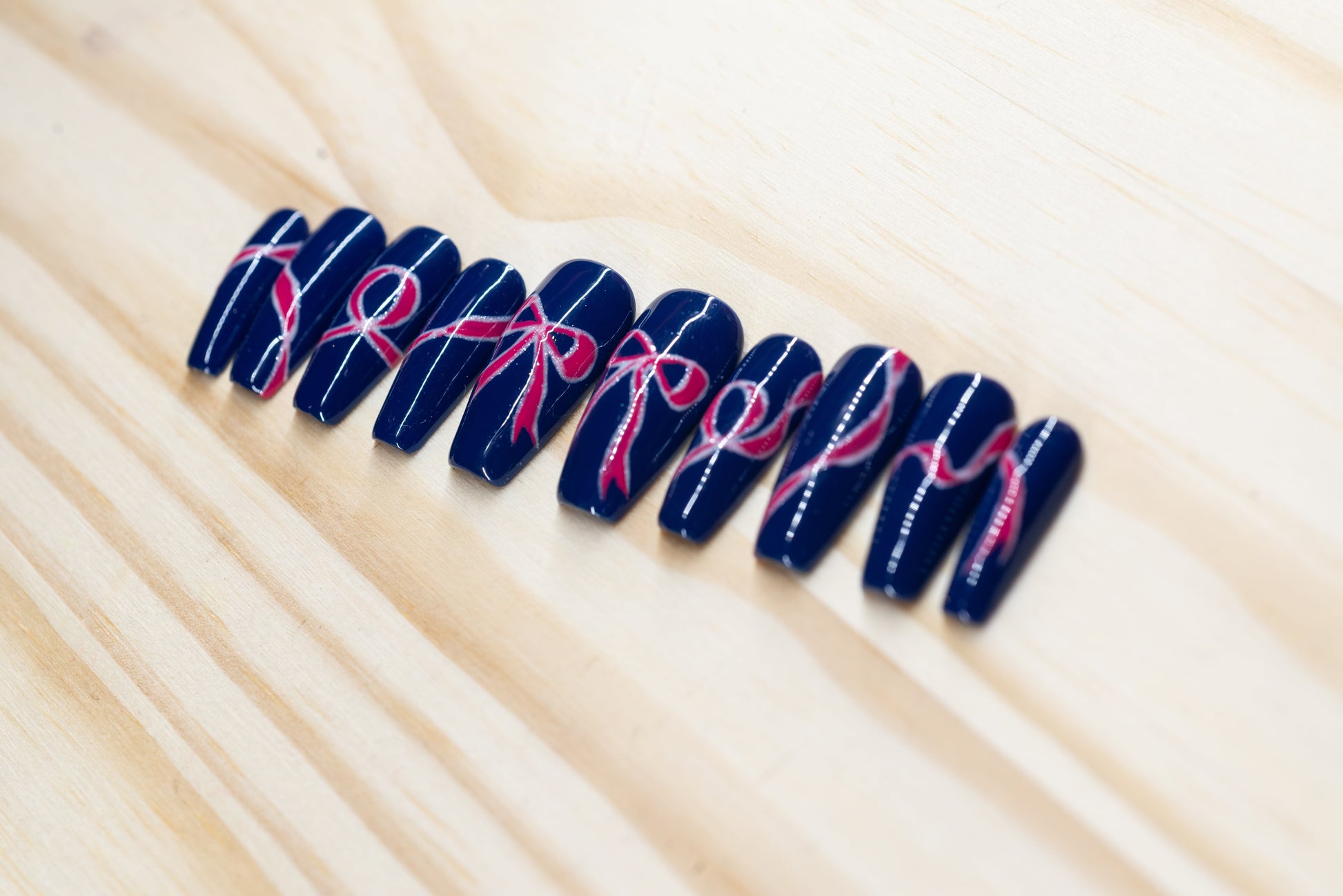 navy blue press on nails with pink bow motif featured on a wooden background