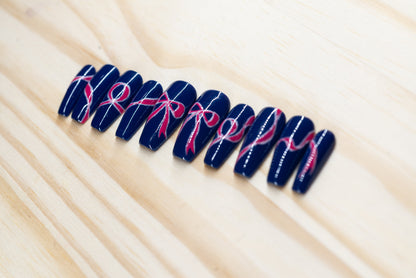 navy blue press on nails with pink bow motif featured on a wooden background