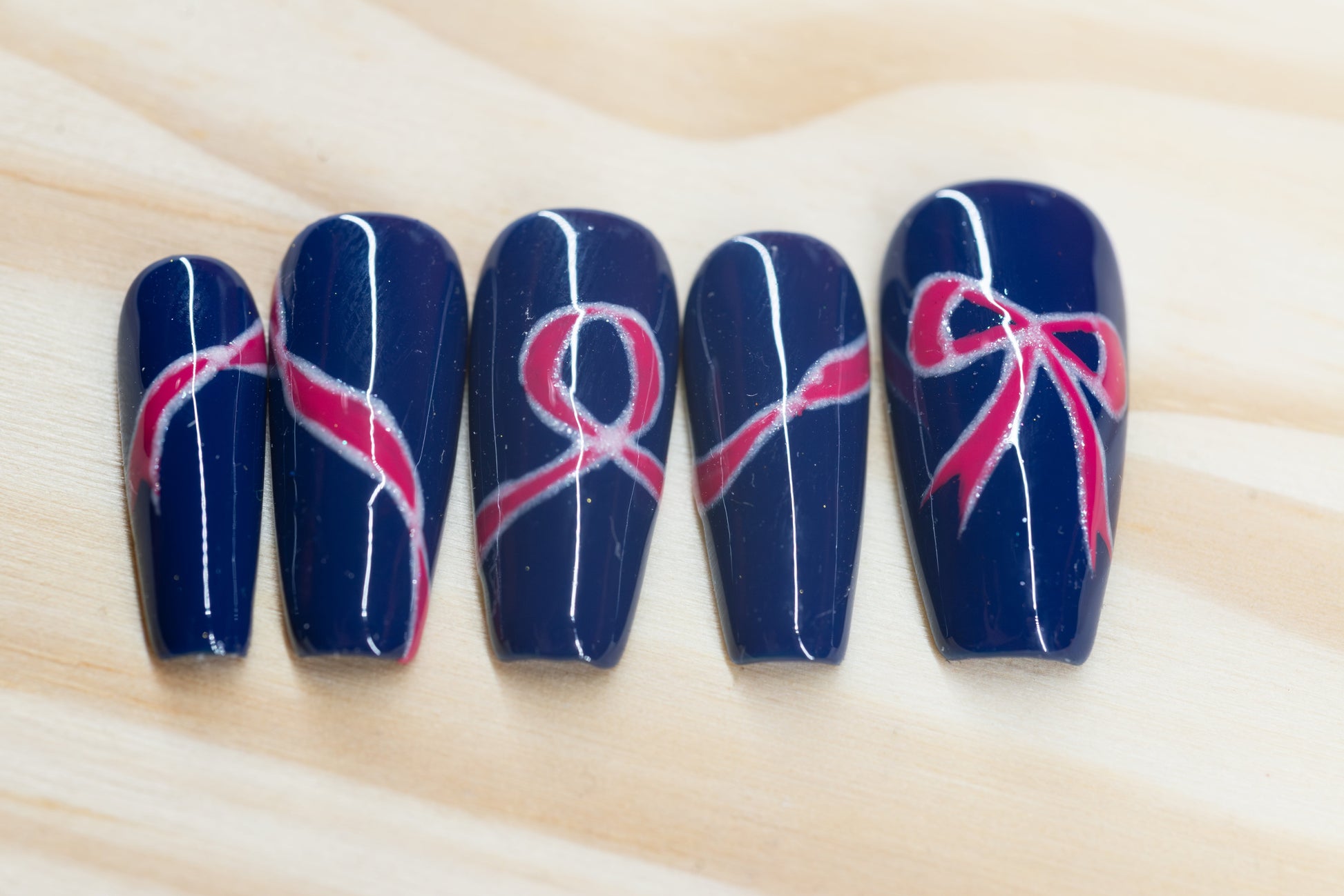 navy blue press on nails with pink bow motif featured on a wooden background