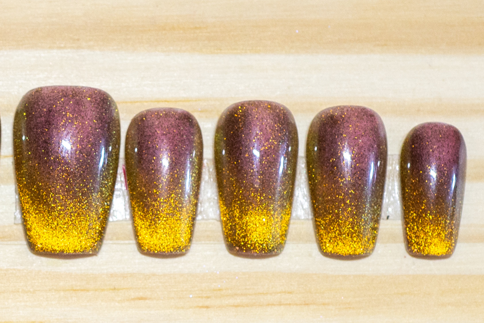 press on nails painted with a tiger-eye colored cat eye polish featured on a wooden background
