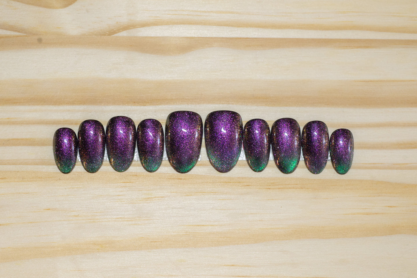 Cat eye press on nails in purple/fuchsia with teal green french tip flash on a wooden background