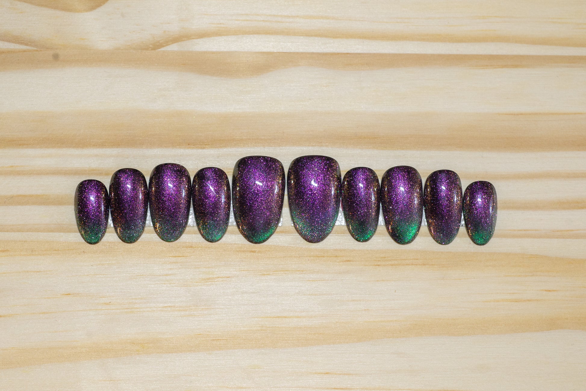Cat eye press on nails in purple/fuchsia with teal green french tip flash on a wooden background