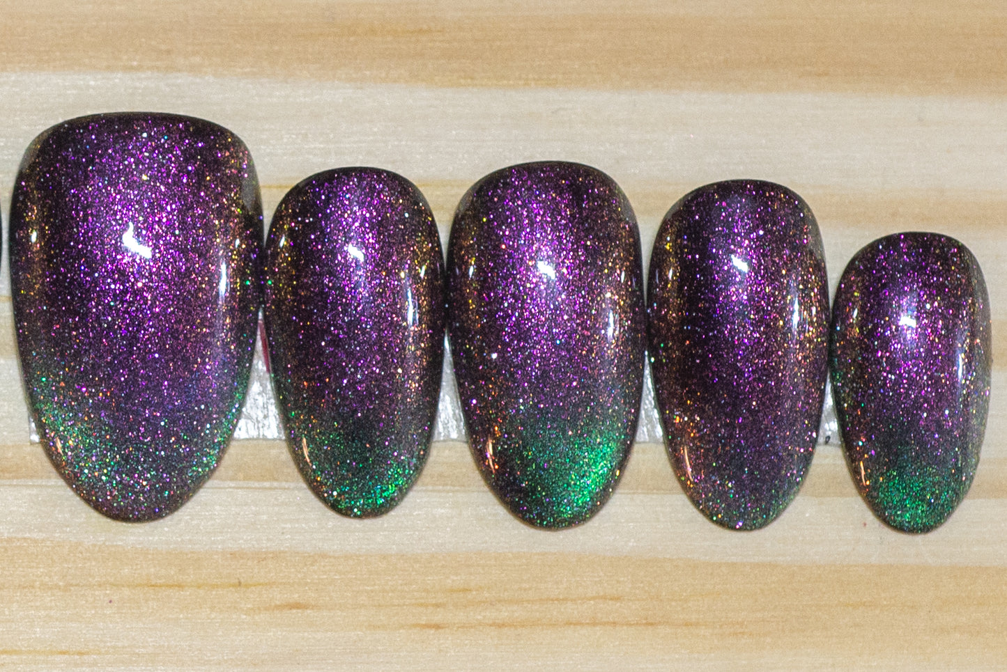 Cat eye press on nails in purple/fuchsia with teal green french tip flash on a wooden background