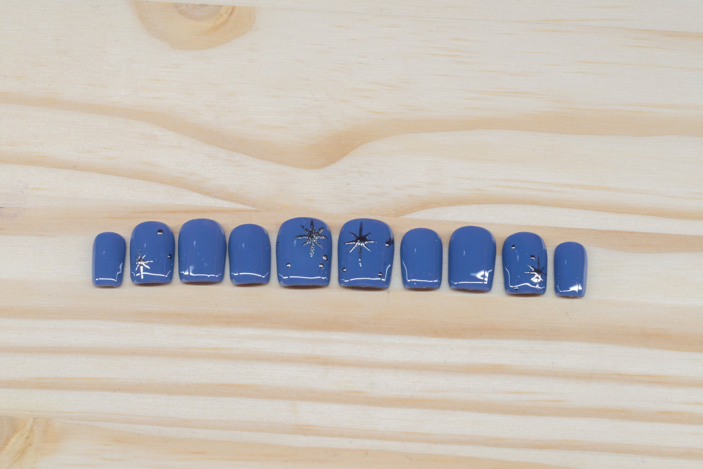 twilight blue press on nails with elegant silver chrome star motif featured on a wooden background