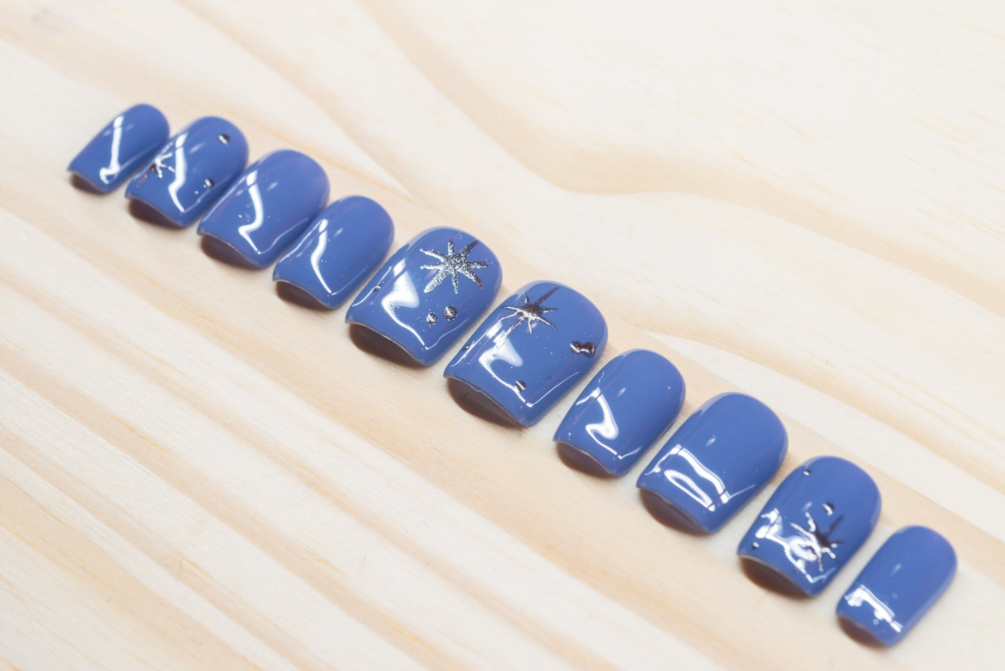 twilight blue press on nails with elegant silver chrome star motif featured on a wooden background