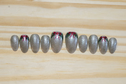 sparkly silver press on nails with  green wreath/swag and red bow detail on 4 nails on a wooden background