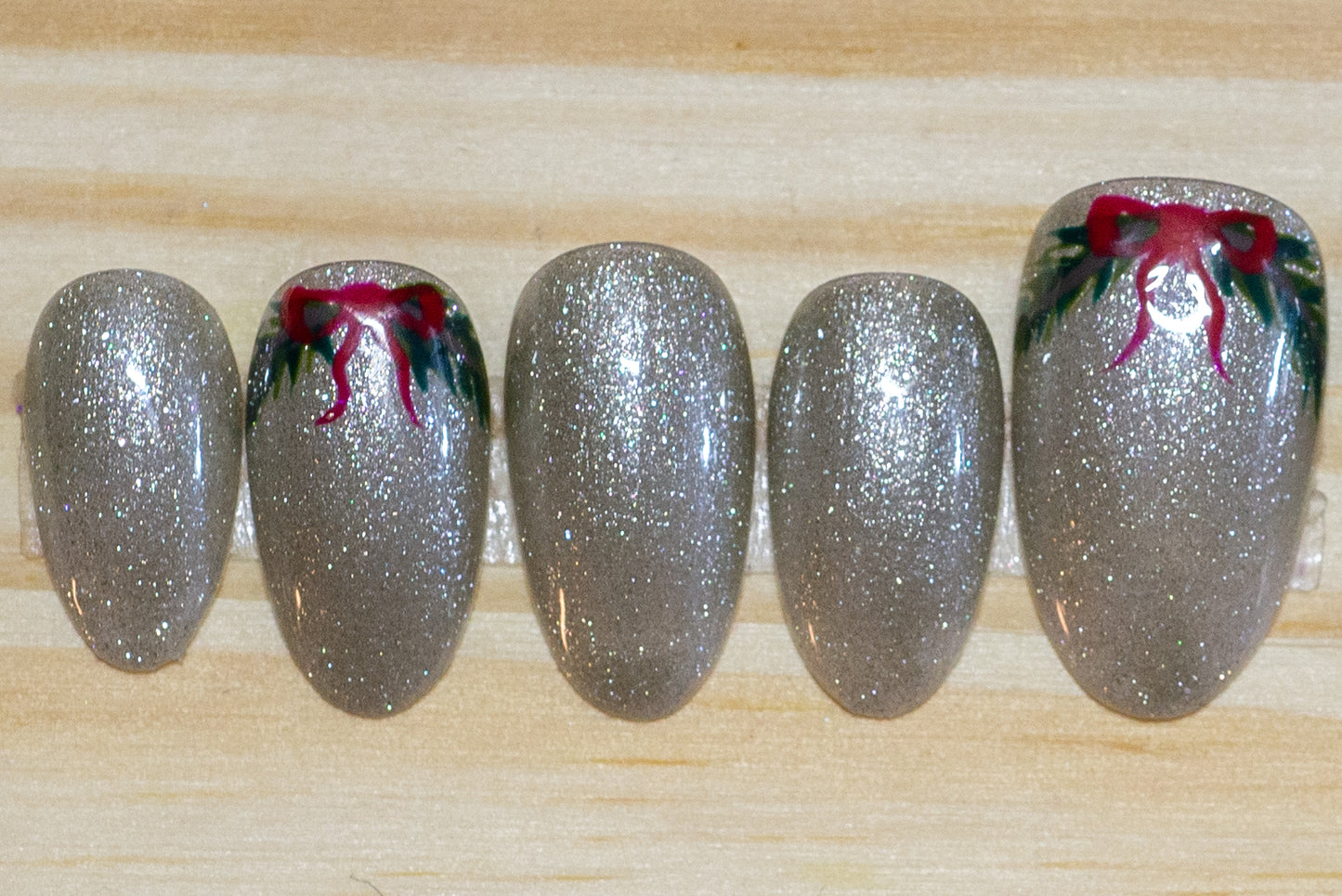 sparkly silver press on nails with  green wreath/swag and red bow detail on 4 nails on a wooden background